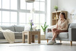 © Pixel-Shot - Happy young woman sitting on grey sofa in interior of light living room