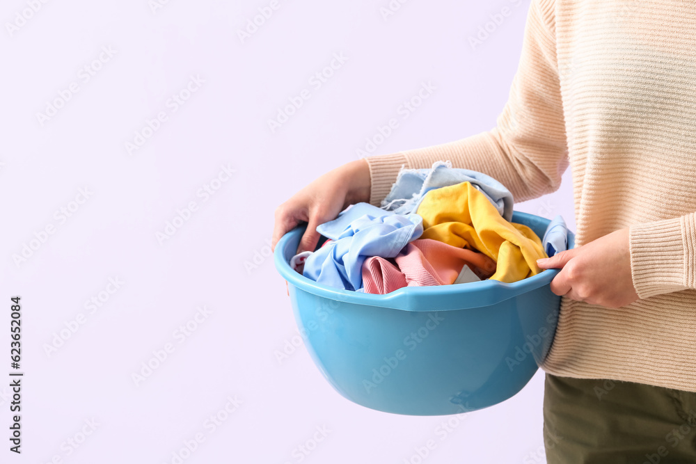 Woman holding plastic basin with dirty laundry on lilac background