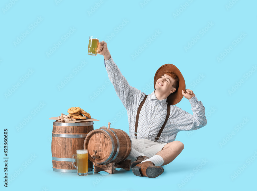 Young man in traditional German clothes with beer and snacks on blue background