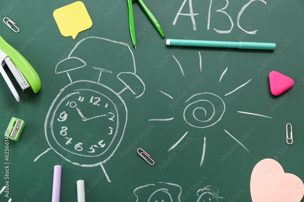 Different stationery and drawings on green chalkboard