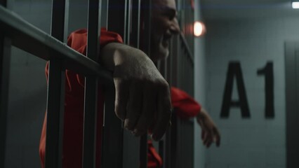 Wall Mural - Elderly prisoner in orange uniform cries, holds his hands on metal bars. Criminal serves term of imprisonment in prison cell. Depressed inmate stands and walks behind bars in jail or detention center.