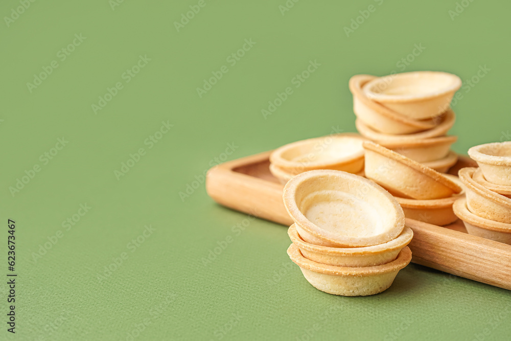 Wooden board with homemade tartlets on green background