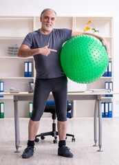 Wall Mural - White bearded old man employee doing exercises in the office