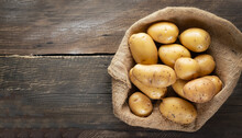 Raw Potato Food . Fresh Potatoes In An Old Sack On Wooden Background. Free Place For Text. Top View