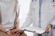 © rogerphoto - Doctor and patient discussing health exam results. Friendly physician reassuring a young woman by one hand while keeping clipboard with medical papers in another. Medicine concept