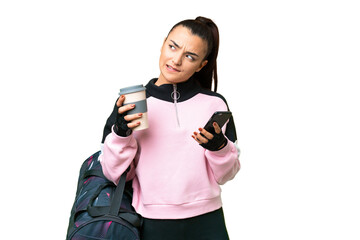 Wall Mural - Young sport woman with sport bag over isolated chroma key background holding coffee to take away and a mobile while thinking something