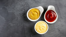 Set Of Three Sauces - Mayonnaise, Mustard And Ketchup In White Ceramic Bowls On Black Stone Or Concrete Background. Selective Focus. Top View.
