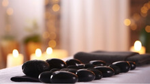 Close Up Shot Of Black Volcanic Stones Laid In Line And A Rolled Towel On The Massage Table In A Spa Salon Room. Bokeh Lights On The Background. Generative AI