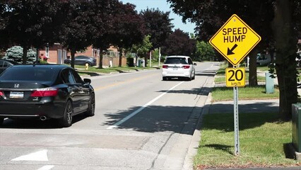 Wall Mural - medium on speed hump arrow 20 km/h sign in black writing on yellow background silver post with cars passing over speed bump