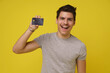Portrait of very excited handsome brunette young 20s man with bank debit card in hand dressed in t-shirt isolated over yellow color background