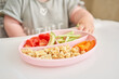 Cute child eats healthy food pasta and vegetables steamed,. Portraits of a cute 10 months old baby girl. The baby sitting in a special high chair for babies. 