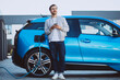 © Petro - Young man charging electric car at home and using mobile phone