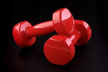 Two red shiny dumbbells on a black matte background. Close-up. Angle view. Selective focus.