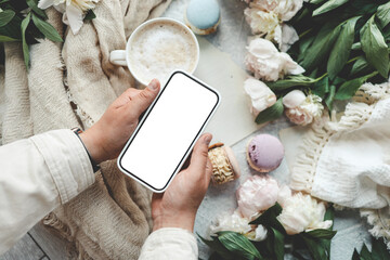 Wall Mural - Phone in hands with an isolated screen on the background of a cup of coffee