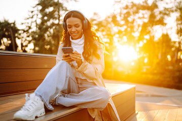 Young woman smiling happy using smartphone and headphones at the cityю Young woman listens to music, audiobook or podcast. Communication in social networks. Lifestyle. 