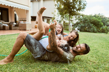 Wall Mural - Young family playing in the backyard with a water hose