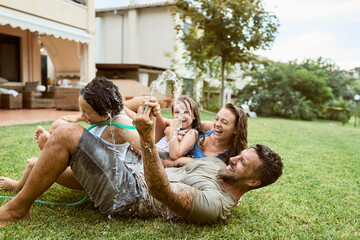 Wall Mural - Young family playing in the backyard with a water hose