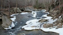 Slow Motion Close Downstream Flyover Of Winter Stream With Snow And Ice.