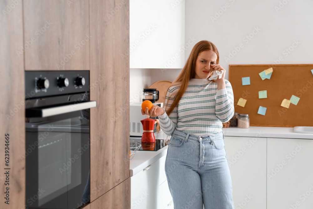 Allergic young woman with tissue and orange in kitchen