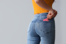 Young Woman With Condom In Pocket On Light Background, Back View