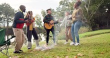 Friends, campfire and guitar with singing, dancing and happy together in nature, woods or park for vacation. Men, women and excited with beer, chat or camping by bonfire for music, forest and holiday