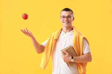 Male student with apple and books on yellow background