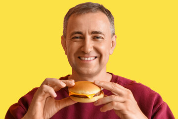 Canvas Print - Mature man eating tasty burger on yellow background, closeup