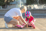 Caucasian woman helping her daughter put on roller skates.