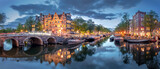 Fototapeta Krajobraz - Amsterdam. Panoramic view of the historic city center of Amsterdam. Traditional houses and bridges of Amsterdam. A blue evening time and the serene reflection of lights in the water. Long exposure. Eu