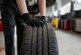 Fototapeta Do przedpokoju - Male mechanic wearing gloves rolling tire for replacement at car service