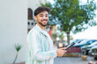 © luismolinero - Handsome Arab man holding a tablet at outdoors smiling a lot