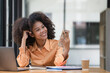 © Songsak C - Portrait of a beautiful confident businesswoman using a laptop computer holding a mobile phone sitting in a modern office. Smiling African American freelancer working online from home.