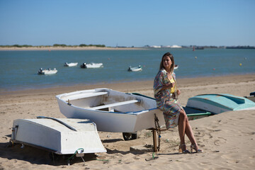 Pretty young blonde woman sitting in the fishermen's boats on the seashore. In the background on the horizon the blue sea and the biosphere reserve of the natural park and the mouth of the river