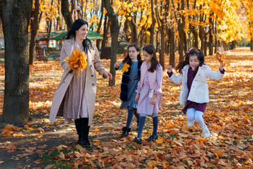 Poster - mother and daughters are in autumn city park, happy people walking together, family with children, playing with yellow leaves, beautiful nature, bright sunny day