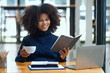 © SOMKID - Happy young African American woman working and sitting at desk in office.