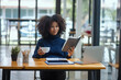 © SOMKID - Happy young African American woman working and sitting at desk in office.