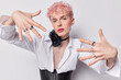 © WHstudio Leushin N - Horizontal shot of young gay man with pink hair demonstrates his unique beauty keeps hands raised shows fingers with rings poses with vivid makeup isolated over white background. Lgbt lifestyle