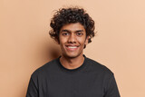 Fototapeta  - Portrait of handsome cheerful man with curly hair smiles toothily poses happy against brown background dressed casually isolated over brown background. Positive human emotions and ethnicity concept