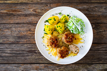 Seared pork meatballs with fried onion, boiled potatoes and lettuce in cream sauce on wooden table
