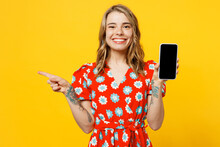 Young Woman Wear Red Dress Casual Clothes Hold In Hand Use Mobile Cell Phone With Blank Screen Workspace Area Point Finger Aside On Area Isolated On Plain Yellow Background Studio. Lifestyle Concept.