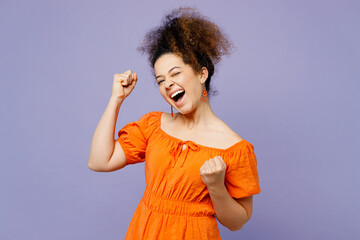 Poster - Young latin woman she wearing orange blouse casual clothes doing winner gesture celebrate clenching fists say yes isolated on plain pastel light purple background studio portrait. Lifestyle concept.