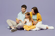 © ViDi Studio - Full body young parents mom dad with child kid daughter girl 6 years old wear blue yellow casual clothes sit hold in hand use mobile cell phone isolated on plain purple background. Family day concept.