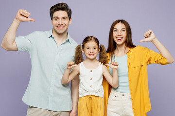 Poster - Young smiling happy parents mom dad with child kid daughter girl 6 years old wear blue yellow casual clothes point thumb fingers on themselves isolated on plain purple background. Family day concept.