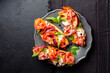 A dark grey plate with with open sandwiches, snack. Toastet bread, griddled peach, parma ham or prosciuto and robiola cheese, with balsamic vinegar and basil. Black background, top view.