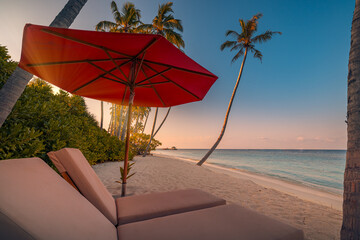 Beautiful tropical sunset coast, two sun beds chairs umbrella under palm trees. Closeup white sand, sea view horizon colorful twilight sky calm and relaxation. Inspire beach resort wellbeing landscape