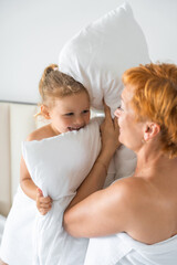 Wall Mural - Young mother and little daughter having fun with pillows on bed