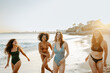 © Prostock-studio - Summertime fun. Group of carefree women friends laughing while running in swimwear at the beach, copy space