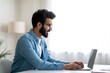 © Prostock-studio - Smiling indian male writer working with laptop at desk in home office