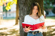 © Minerva Studio - Female student reading a book outdoor in the park lying