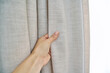 Light beige sand linen natural curtains on window, close-up of hand touching curtains